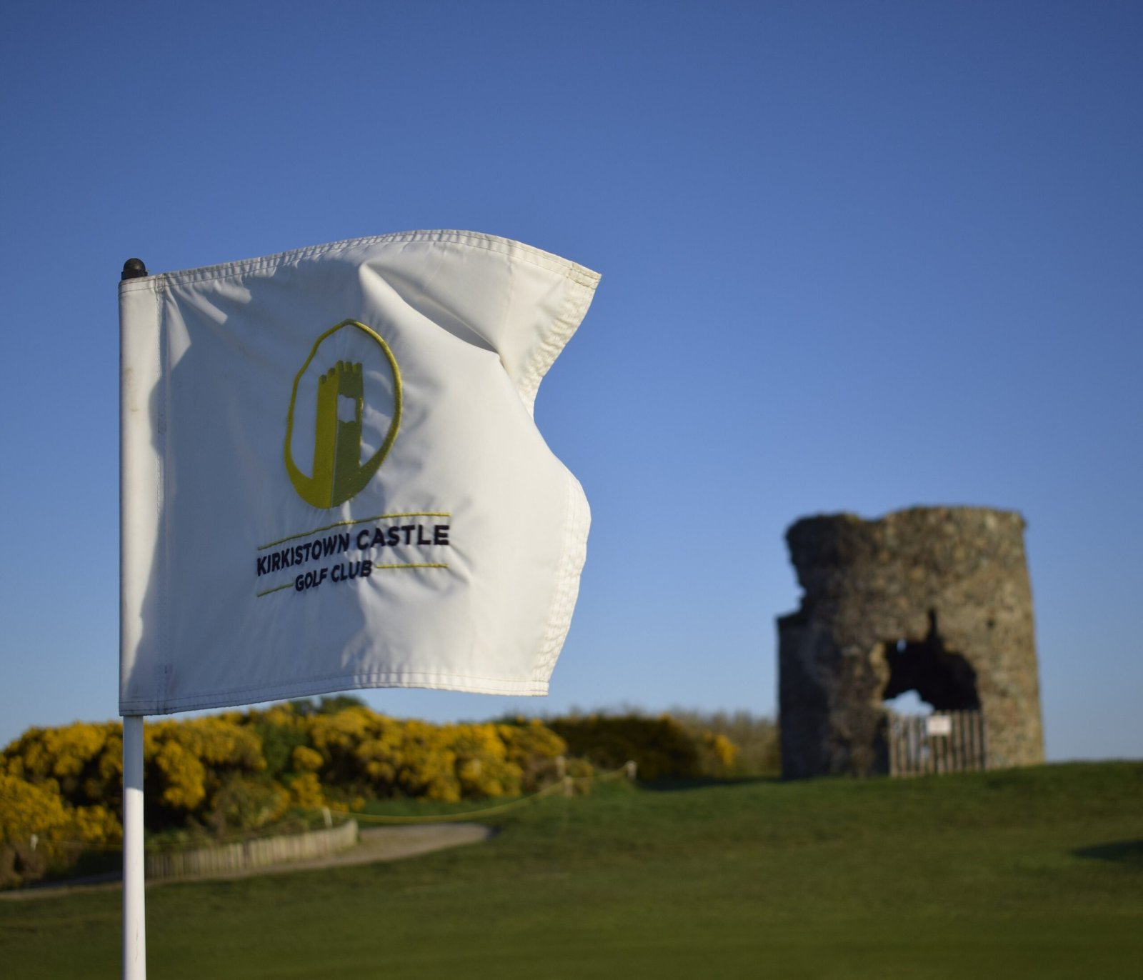 The Kirkistown Castle Golf Club flag on the green with the castle ruins in the background